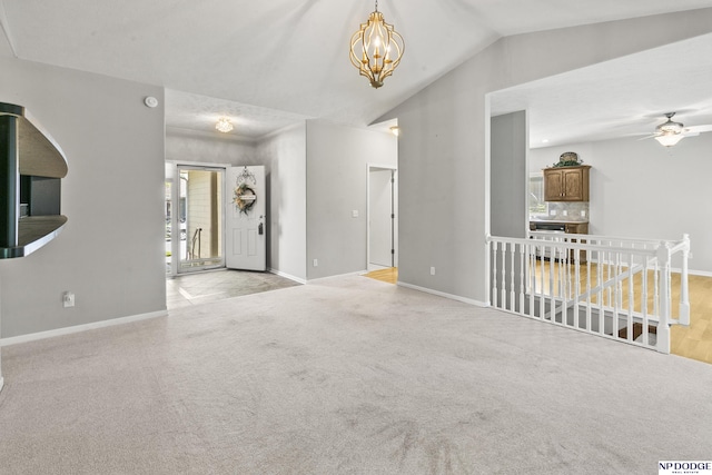 unfurnished living room featuring lofted ceiling, ceiling fan with notable chandelier, baseboards, and carpet floors