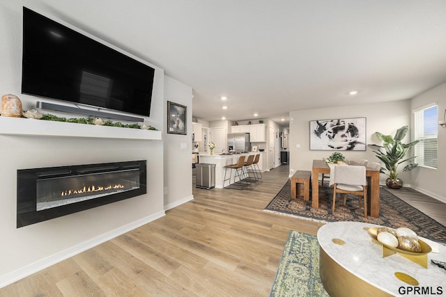 living area featuring light wood finished floors, baseboards, a glass covered fireplace, and recessed lighting