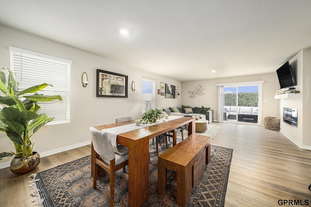 dining room featuring light wood finished floors, baseboards, a glass covered fireplace, and recessed lighting