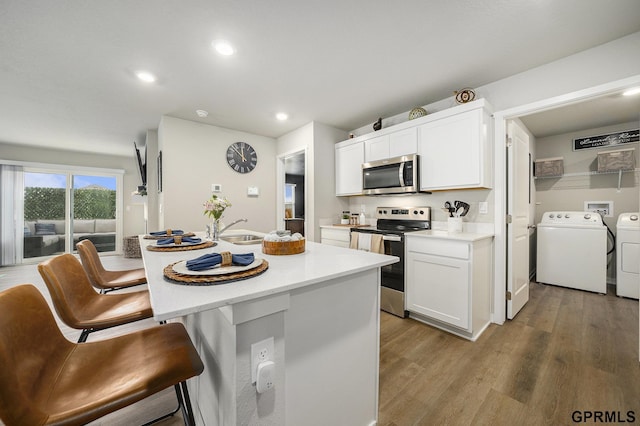 kitchen featuring a breakfast bar area, light countertops, a sink, stainless steel appliances, and independent washer and dryer
