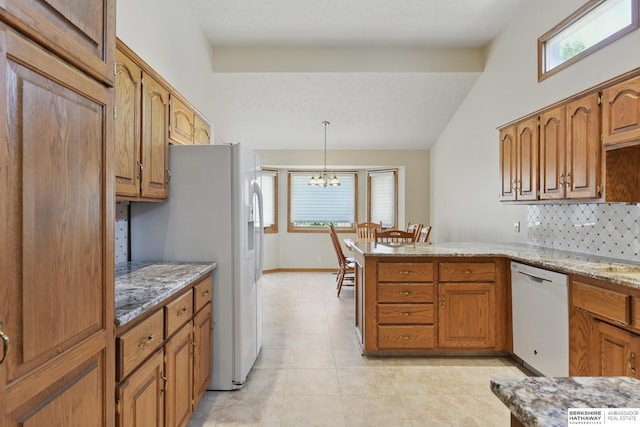 kitchen featuring white appliances, a peninsula, a chandelier, light stone countertops, and tasteful backsplash