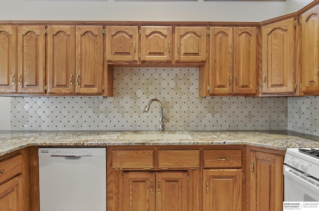 kitchen with white appliances, a sink, tasteful backsplash, brown cabinetry, and light stone counters