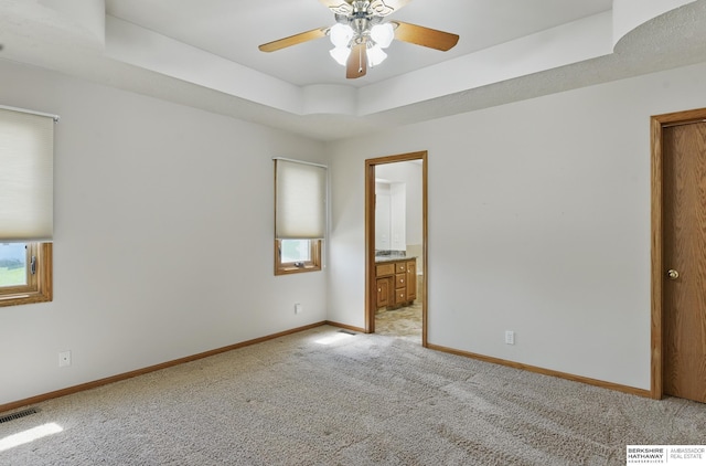 empty room with light carpet, baseboards, ceiling fan, and a tray ceiling