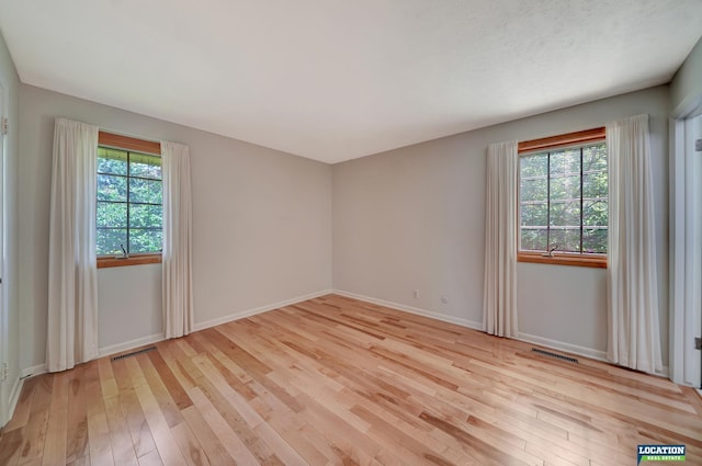 spare room with light wood finished floors, visible vents, and baseboards