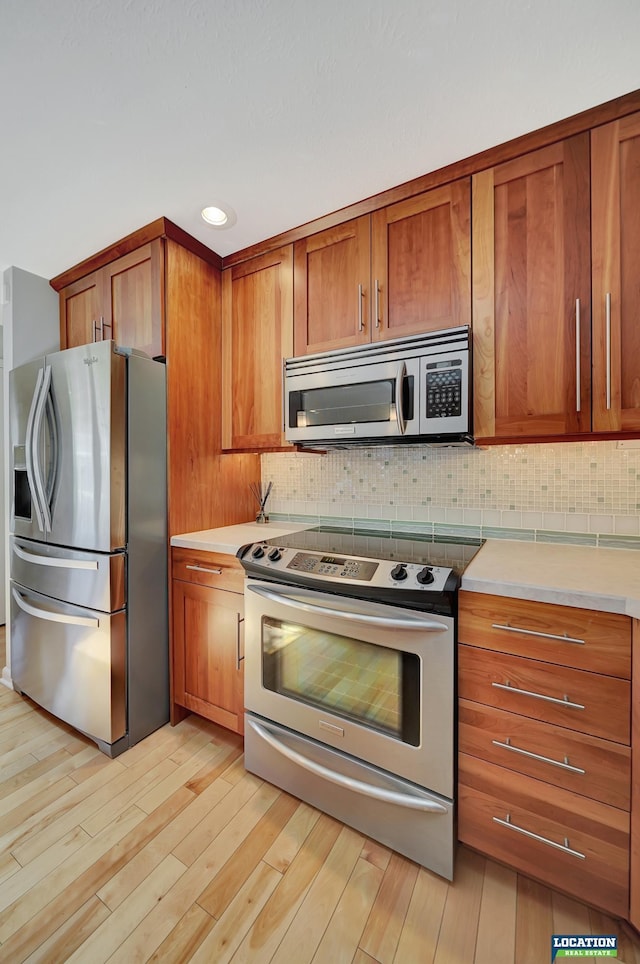 kitchen featuring brown cabinetry, backsplash, light countertops, and appliances with stainless steel finishes
