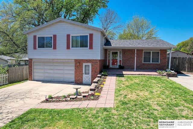 tri-level home with driveway, brick siding, fence, an attached garage, and a front yard