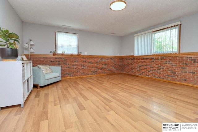 unfurnished room featuring a wealth of natural light, brick wall, light wood-type flooring, and wainscoting