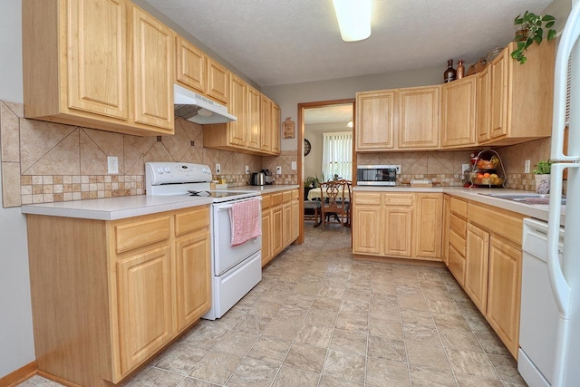 kitchen with light brown cabinetry, under cabinet range hood, white appliances, backsplash, and light countertops