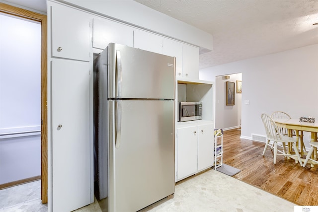 7545 Sherman Dr, Omaha, NE 68134 - kitchen featuring freestanding refrigerator, stainless steel microwave, white cabinets, light wood-style flooring, and baseboards