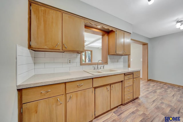 kitchen with a sink, baseboards, light countertops, light wood-style floors, and tasteful backsplash