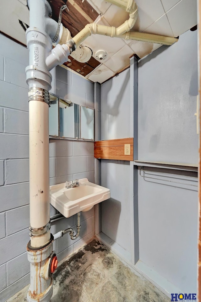 bathroom featuring unfinished concrete floors, concrete block wall, and a sink