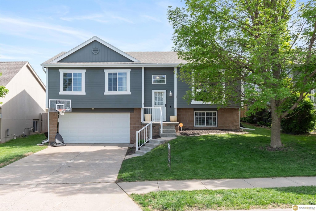 raised ranch featuring a garage, driveway, a front lawn, and a shingled roof