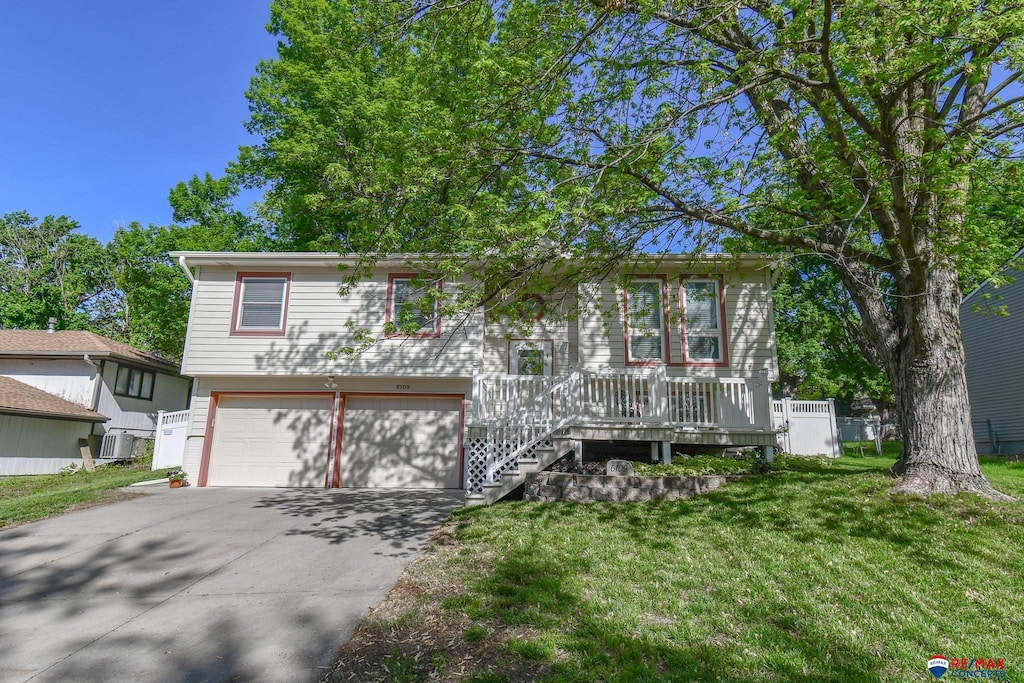 raised ranch with a garage, driveway, a front yard, central AC unit, and a porch