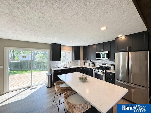 kitchen featuring stainless steel appliances, a sink, a kitchen bar, a textured ceiling, and backsplash