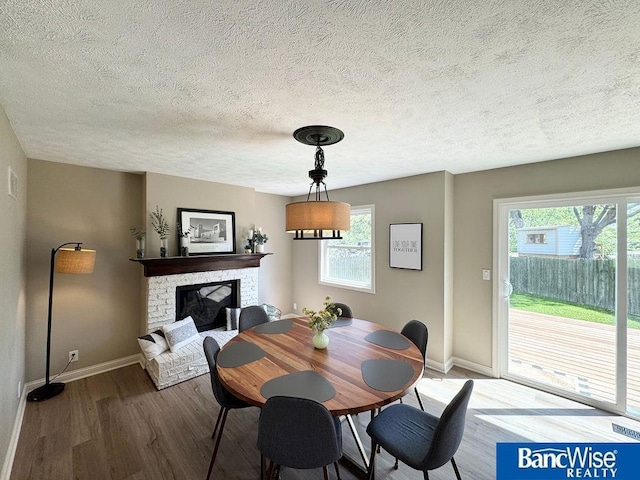 dining area featuring wood finished floors, baseboards, a textured ceiling, and a brick fireplace