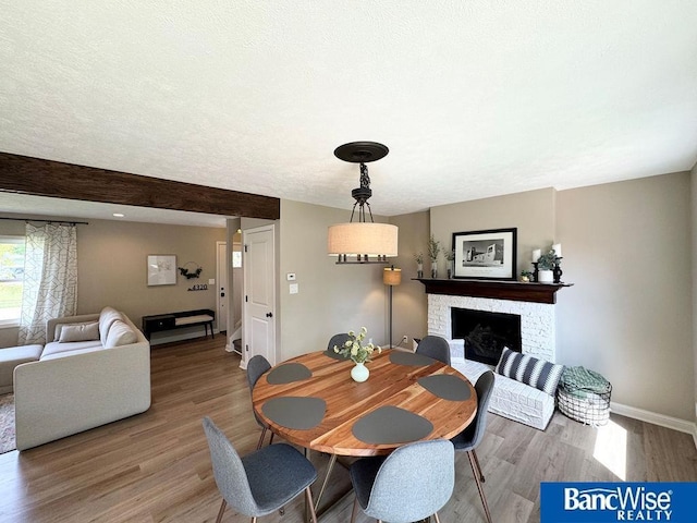 dining room featuring baseboards, light wood-style floors, and a fireplace with raised hearth