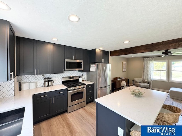 kitchen with appliances with stainless steel finishes, tasteful backsplash, open floor plan, light wood finished floors, and a center island