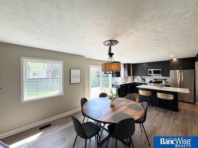dining area featuring light wood finished floors, baseboards, and a textured ceiling
