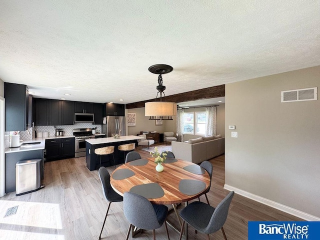 dining area featuring a textured ceiling, light wood-style floors, and baseboards