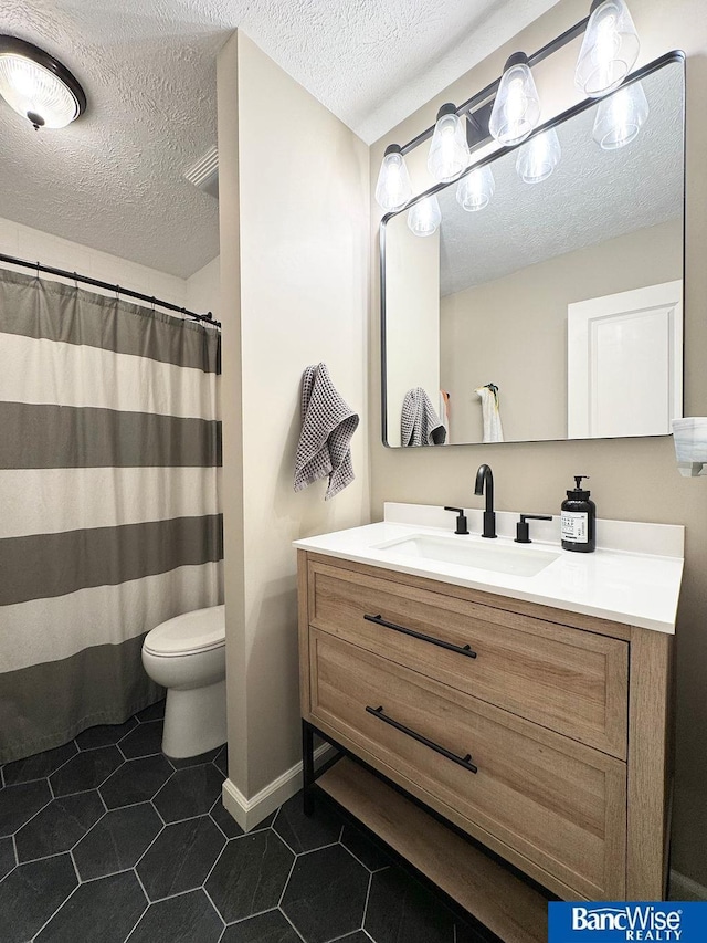 bathroom featuring a textured ceiling, vanity, tile patterned flooring, toilet, and baseboards