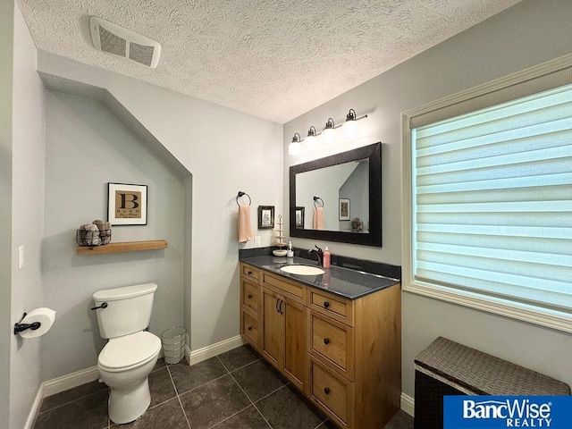 bathroom with vanity, toilet, tile patterned floors, a textured ceiling, and baseboards