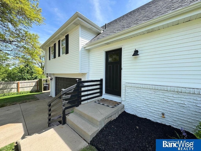 view of exterior entry featuring fence, an attached garage, and a shingled roof