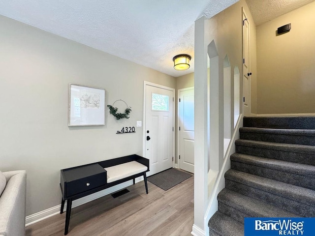 entrance foyer featuring a textured ceiling, light wood finished floors, stairs, and baseboards