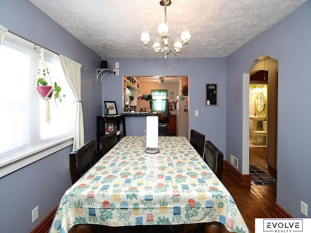 dining space featuring hardwood / wood-style floors, a chandelier, arched walkways, a textured ceiling, and baseboards
