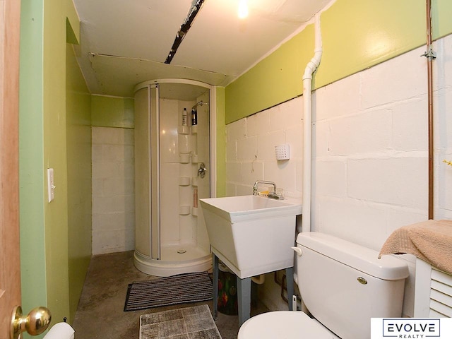 bathroom with concrete flooring, concrete block wall, a shower stall, toilet, and a sink