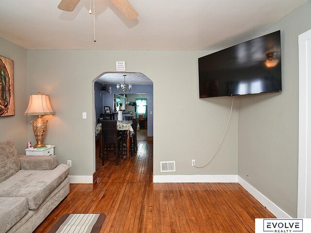 living area featuring arched walkways, wood-type flooring, baseboards, ceiling fan, and a chandelier
