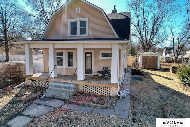 view of front of home featuring covered porch, a gambrel roof, a shed, an outbuilding, and a chimney