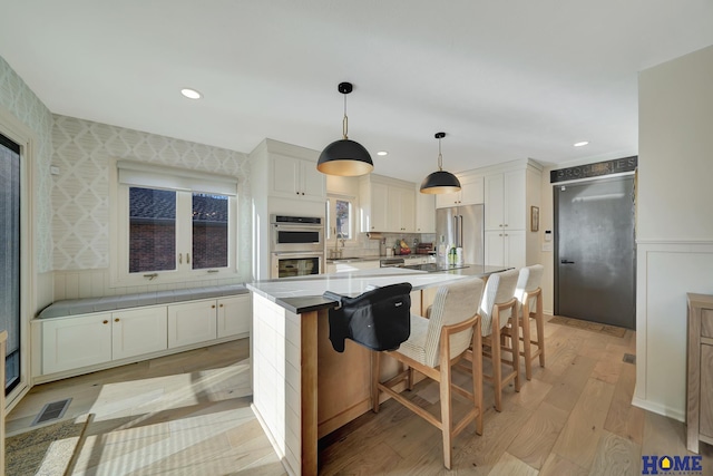 kitchen featuring stainless steel appliances, light wood-type flooring, a sink, a kitchen island, and white cabinetry