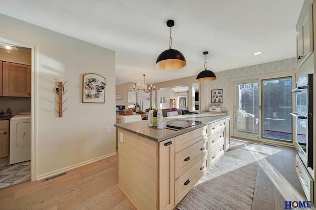 kitchen with washer / dryer, a chandelier, light wood finished floors, a kitchen island, and open floor plan
