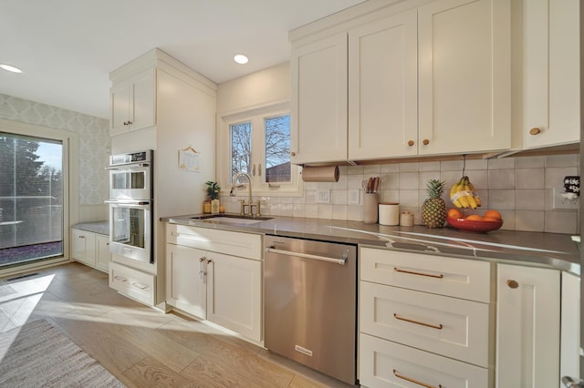 kitchen featuring stainless steel counters, a sink, stainless steel appliances, decorative backsplash, and white cabinets