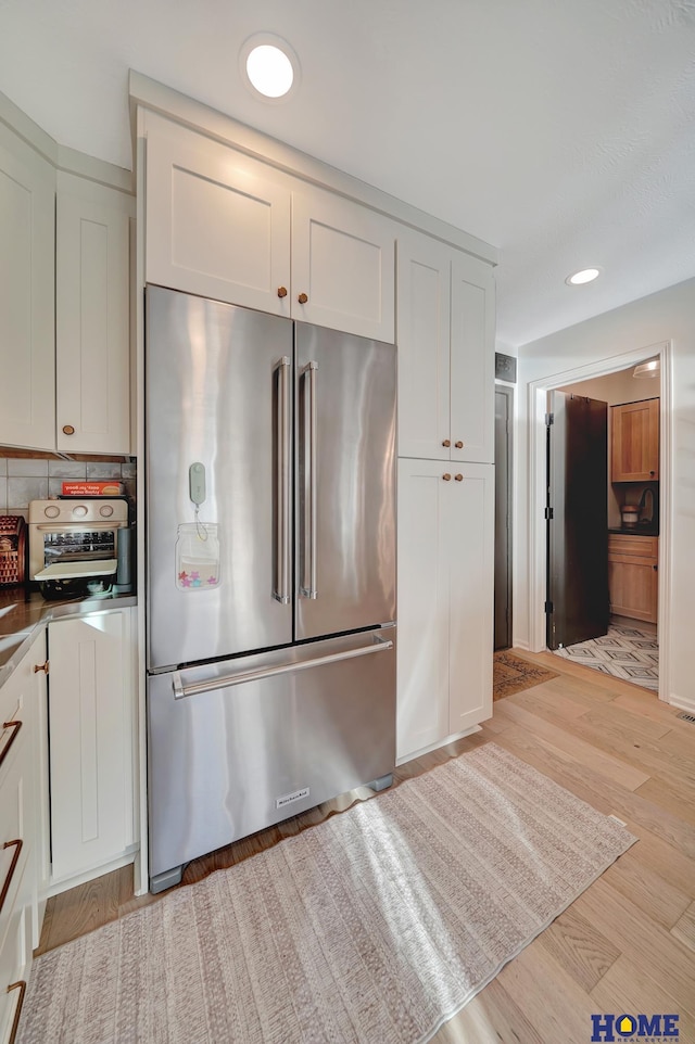 kitchen featuring stainless steel refrigerator, light wood-type flooring, backsplash, white cabinetry, and recessed lighting