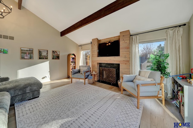 living room with plenty of natural light, beamed ceiling, light wood-type flooring, a fireplace, and a chandelier