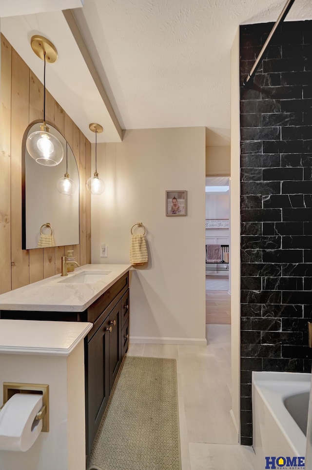 bathroom featuring vanity, a bathtub, baseboards, and a shower