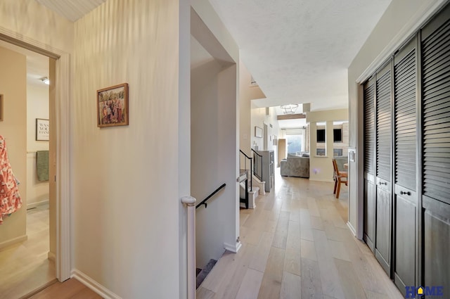 hall featuring light wood finished floors, baseboards, and stairway