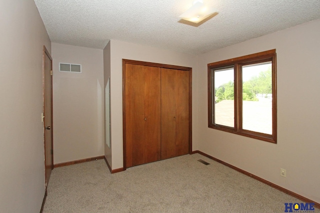 unfurnished bedroom with a closet, light carpet, baseboards, and a textured ceiling