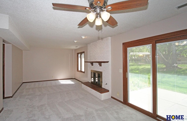 unfurnished living room with light colored carpet, a ceiling fan, a fireplace, a textured ceiling, and baseboards
