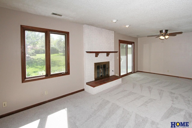 unfurnished living room featuring light colored carpet, ceiling fan, a textured ceiling, a brick fireplace, and baseboards