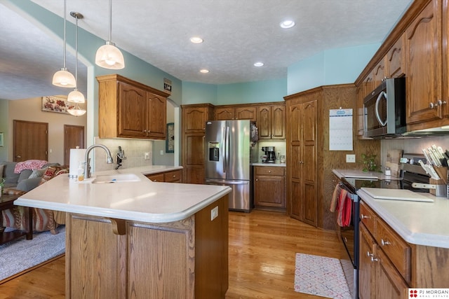kitchen with appliances with stainless steel finishes, a sink, a peninsula, brown cabinets, and recessed lighting
