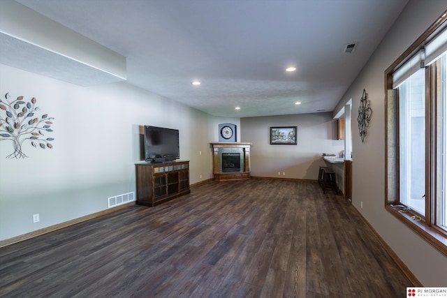 unfurnished living room with dark wood finished floors, a fireplace with raised hearth, recessed lighting, and baseboards