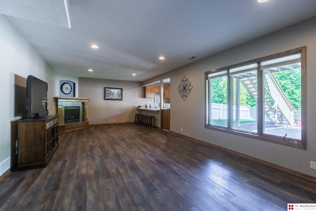 unfurnished living room featuring dark wood-style flooring, a tile fireplace, recessed lighting, and baseboards