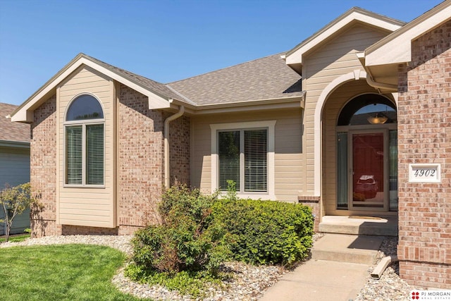 property entrance featuring roof with shingles and brick siding