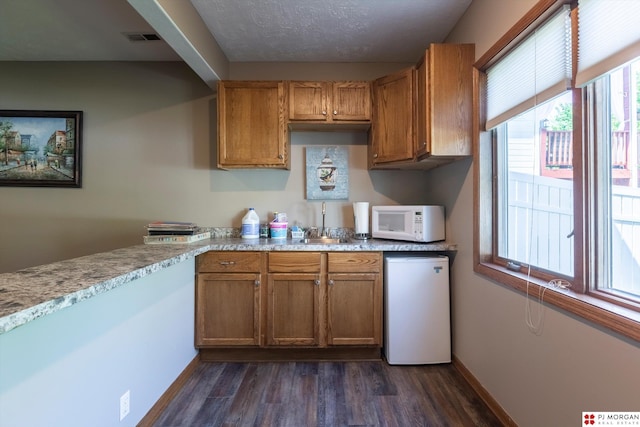 kitchen with white microwave, dark wood-style flooring, and brown cabinets