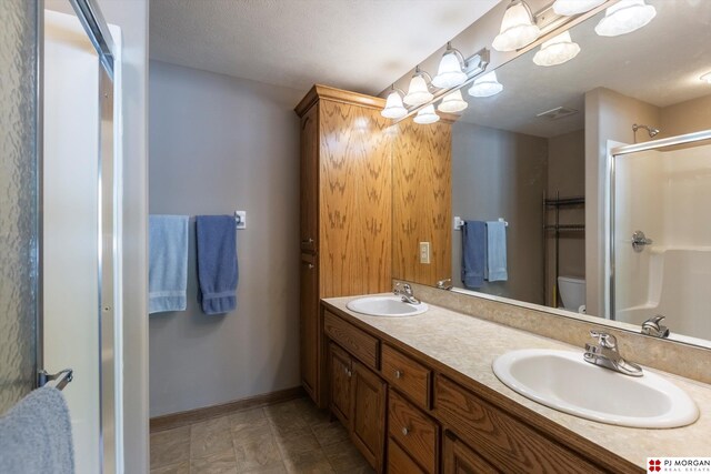 full bathroom with a stall shower, baseboards, double vanity, and toilet