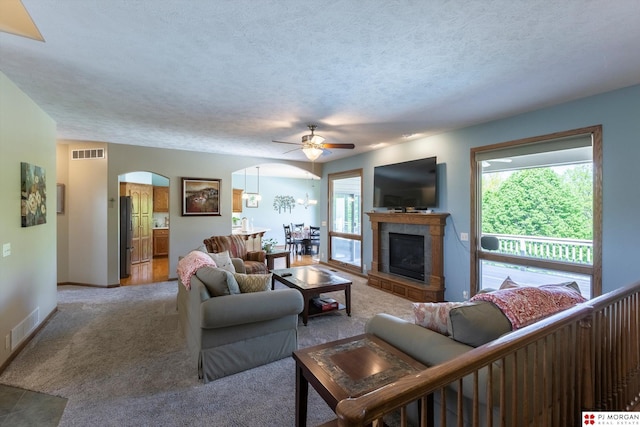 living area featuring arched walkways, a ceiling fan, plenty of natural light, light carpet, and a textured ceiling