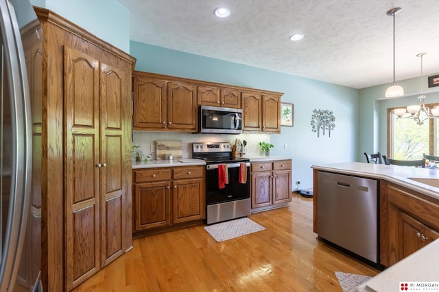 kitchen featuring stainless steel appliances, brown cabinetry, light countertops, a chandelier, and a textured ceiling