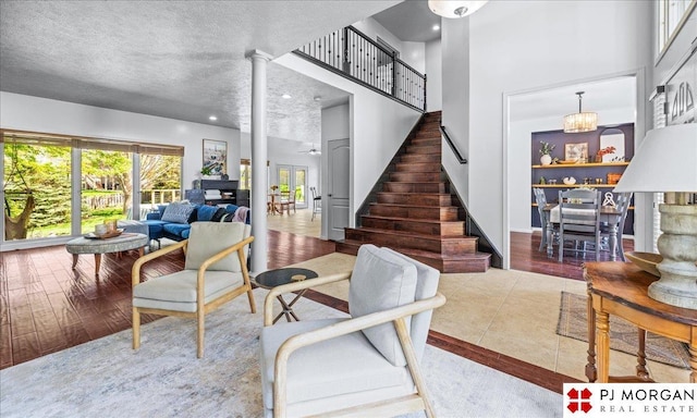 living area featuring stairway, ornate columns, a high ceiling, and wood finished floors